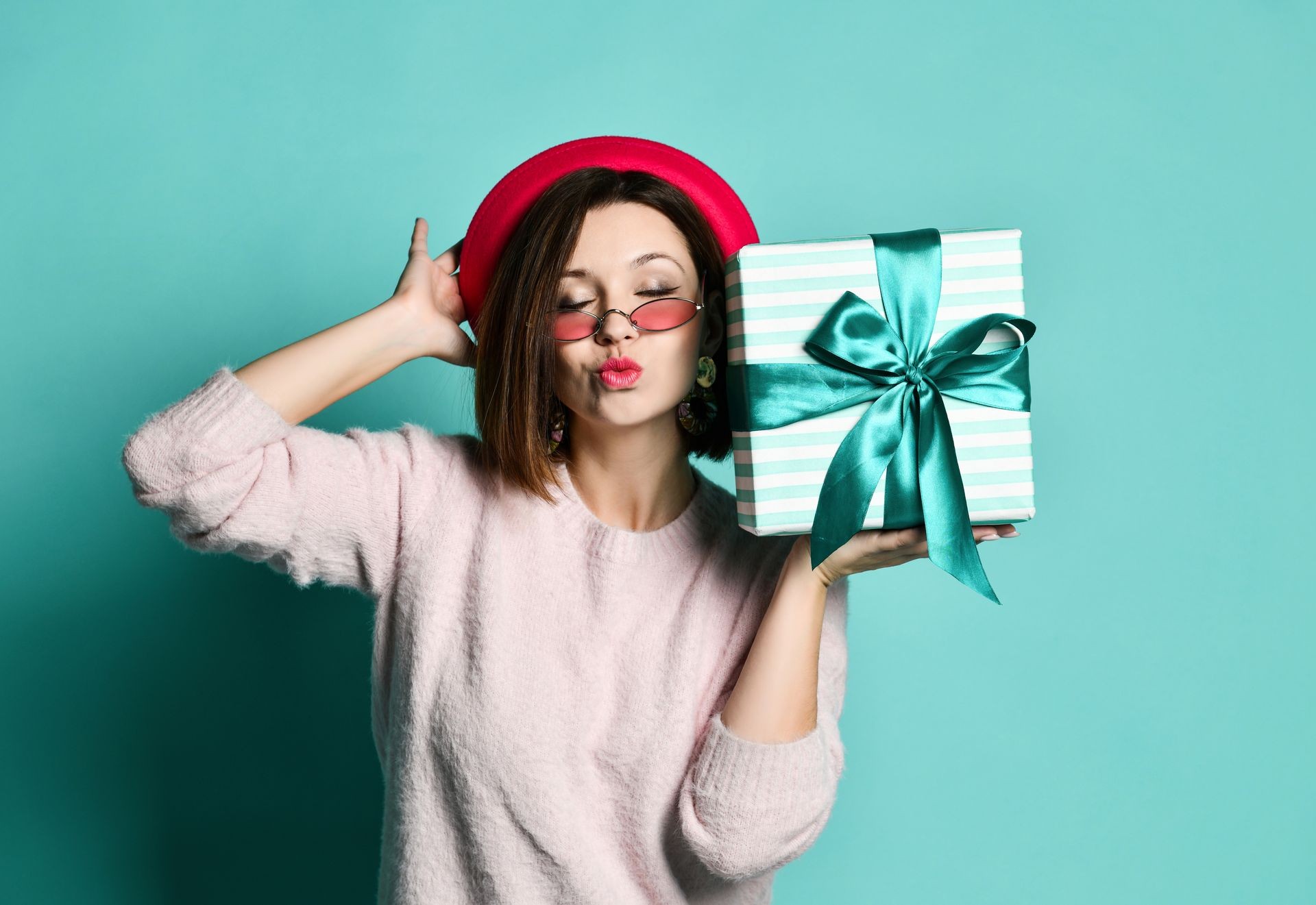 Photo of beautiful woman in felt hat holding present gift box and sending a kiss, isolated over blue background