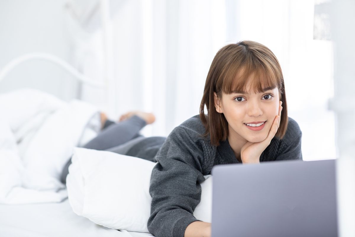 Beautiful Attractive Asian young woman lying on bed and using computer laptop for using social media and shopping online relax in bedroom in holiday,Lifestyle in bedroom Concept